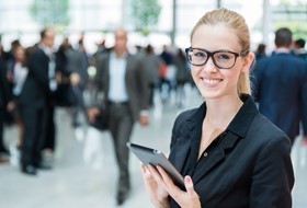 Bild: Geschäftfrau mit Tablet, im Hintergrund viele andere Geschäftsleute